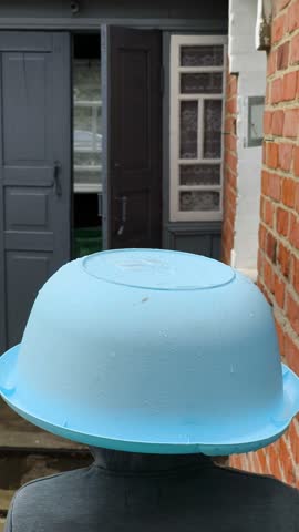 Water droplets splash onto a blue plastic bowl worn on a person