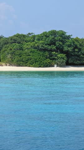 Small, lush green island with a white sand beach and turquoise water in the foreground, Maldives