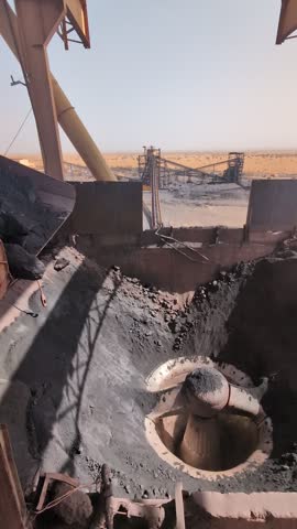 Large pile of dark, rocky material being dumped into a deep pit within an industrial setting, Mauritania