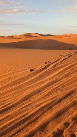 Vast desert landscape with rolling sand dunes under a partly cloudy sky