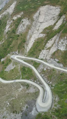 Winding mountain road with multiple switchbacks, carved into the side of a steep, green and rocky mountain
