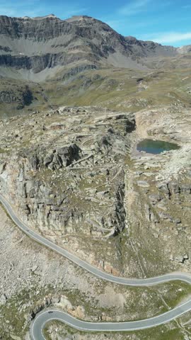 Winding mountain road and a small, dark blue lake nestled among rocky, barren terrain