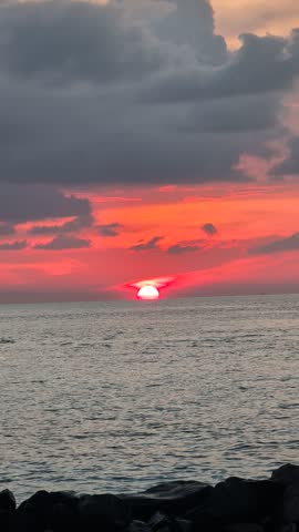 Vibrant red and orange sunset over the ocean, with the sun partially obscured by a dark cloud band