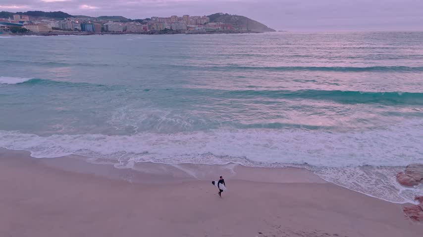 Surfer walking on a sandy beach at dusk in a coruna