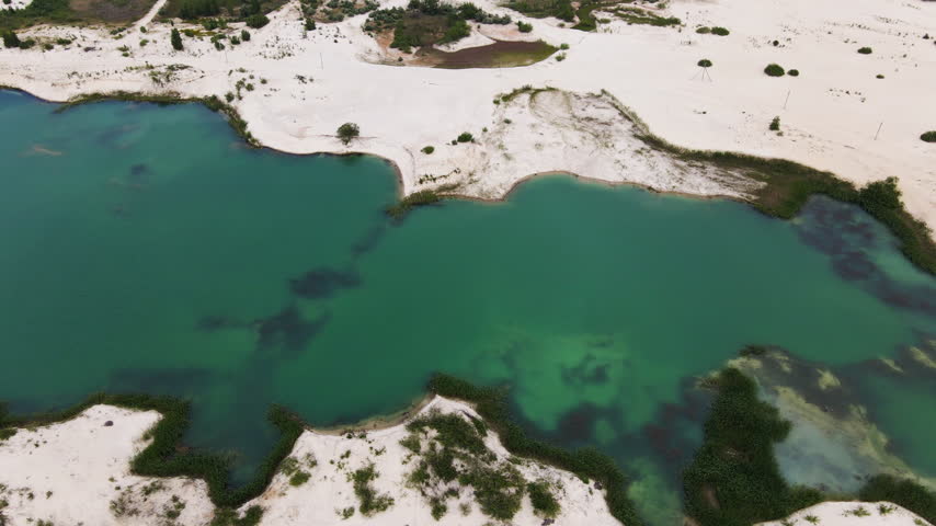 Aerial drone flying over a turquoise quarry lake surrounded by white sand shores and green vegetation
