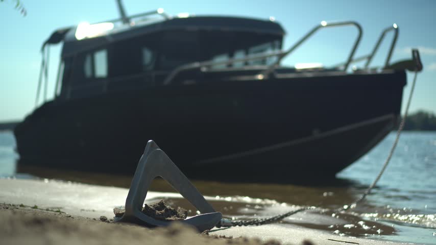 Small Anchor on Chain by the Shore. Black Boat Anchored in Sunny Coastal Weather. Close-Up Coastal Scene.
