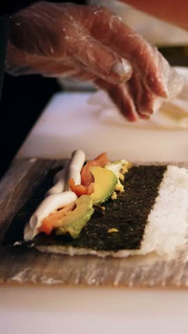 Traditional Japanese food. close-up. Making Sushi Rolls at professional kitchen of sushi bar or restaurant. Sushi Chefs hands are wrapping the nori sheet with ingredients.