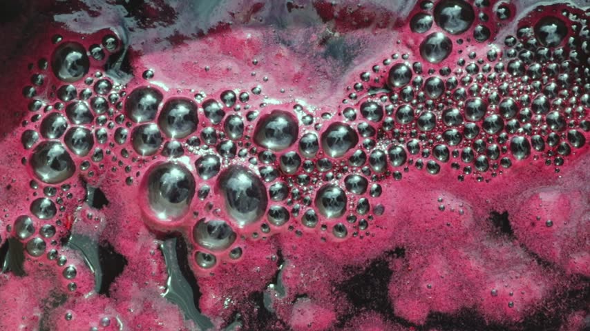 A beautiful abstract image of bubbling foam moving on the surface of freshly squeezed grape juice in a saucepan in a backyard on a rainy autumn day. Extreme close-up, overhead view, slow motion. Concept: traditional local winemaking, retro technology, home winemaking.