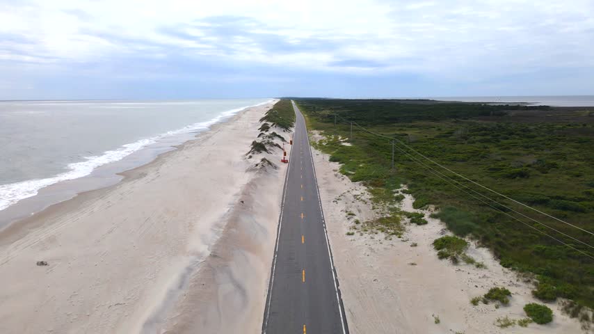Sand dunes border a paved road along the North Carolina ocean shoreline.
