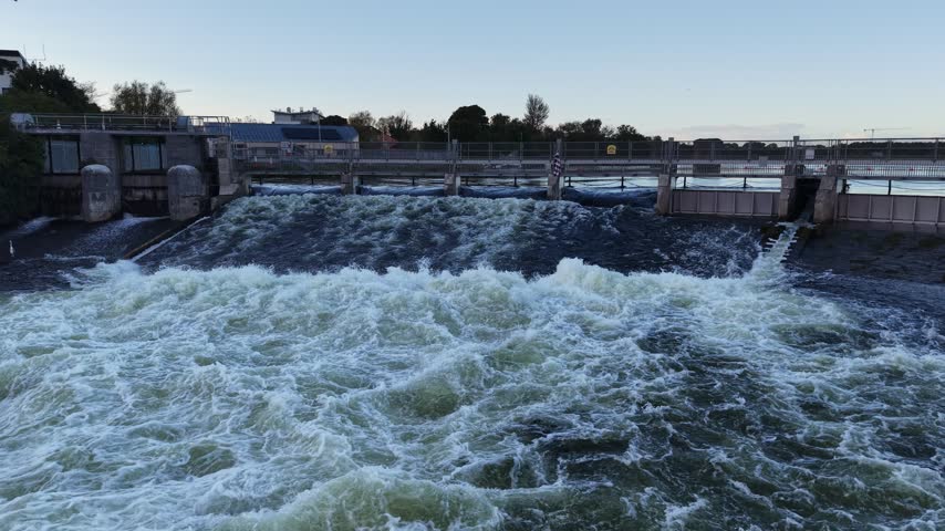 Powerful water flows through Salmon Weir on the River Corrib in Galway City Ireland, creating turbulent whitewater below the weir gates.