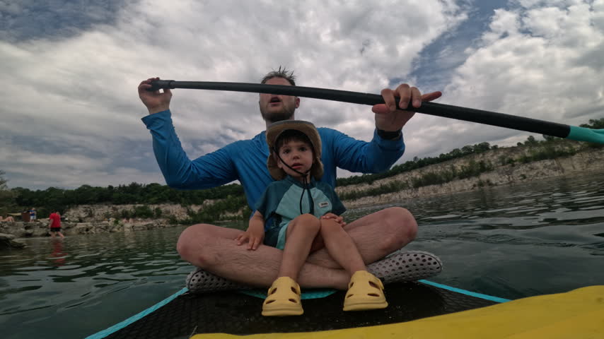 Father paddles and pauses to look around while his smiling son sits in front during their lake outing at Zakrzowek in Krakow, Poland.