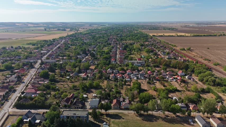 Lőrinci Selyp in Heves County, Hungary, with residential streets, railway lines, fields and meadows surrounding the rural townscape in summer, captured in aerial view.