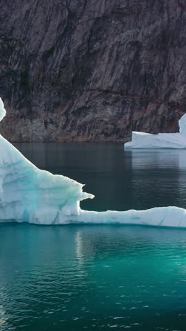 An Inflatable Motorised Boat Travels Among Icebergs In The Greenland Sea, Surrounded By Remote Arctic Waters. Vertical, Aerial Rotating Shot