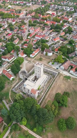 Kinizsi Castle in Nagyvázsony, Hungary, medieval fortress with stone walls and tower above the village center and red rooftops in Veszprém County, viewed by drone.