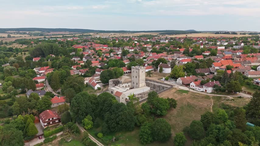Kinizsi Castle in Nagyvázsony, Hungary, medieval fortress with stone walls and tower above village rooftops and greenery in summer, viewed by drone.