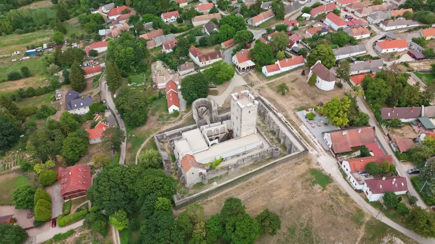 Kinizsi Castle in Nagyvázsony, Hungary, medieval fortress with stone walls and tower amid greenery and village landscape in Veszprém County, captured in aerial view.