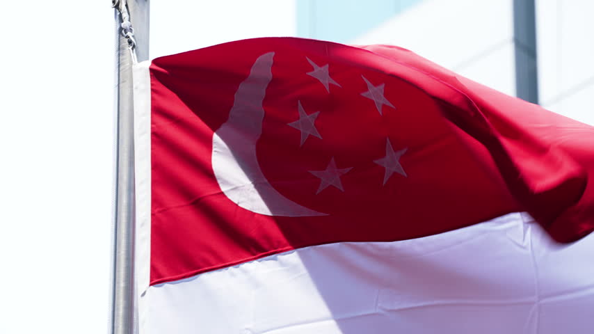 Singapore national flag waving proudly against an urban building exterior backdrop.
