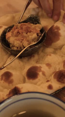 Close-up of hands tearing freshly baked naan flatbread, served with savory dip in a restaurant.