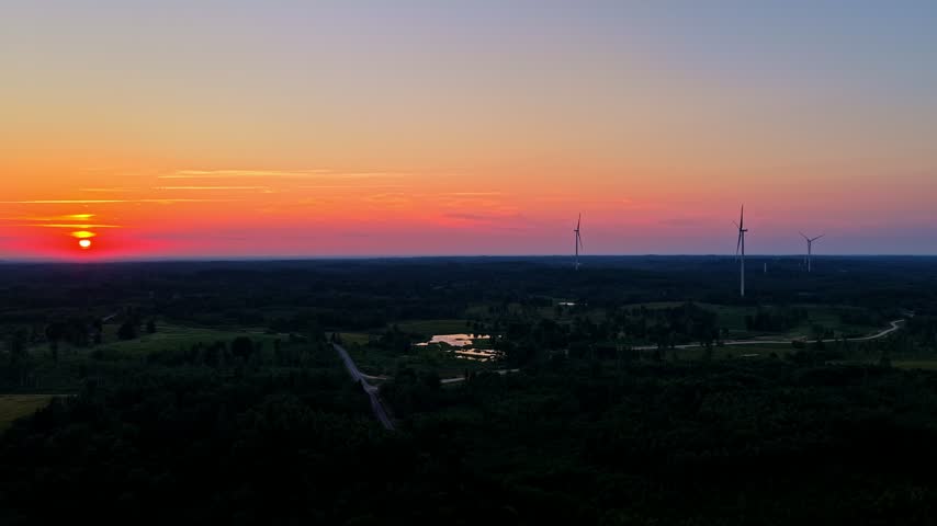Aerial view of a wind farm silhouette with turning blades during a colorful and vibrant sunset