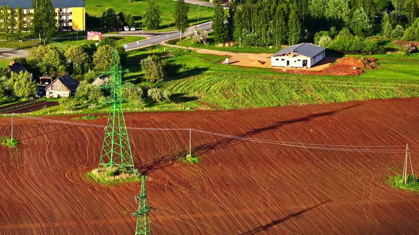 High voltage power lines traversing a plowed agricultural field near a rural town