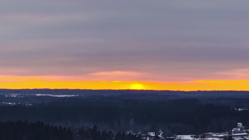 Bright sun setting behind a silhouetted forest with snow covering the land on a winter evening