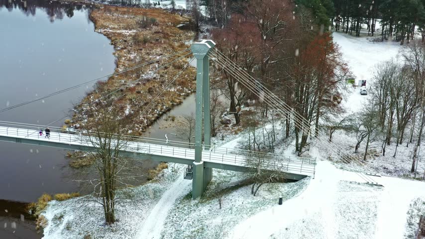 People walking on a pedestrian bridge during a snowfall in a winter park - aerial view