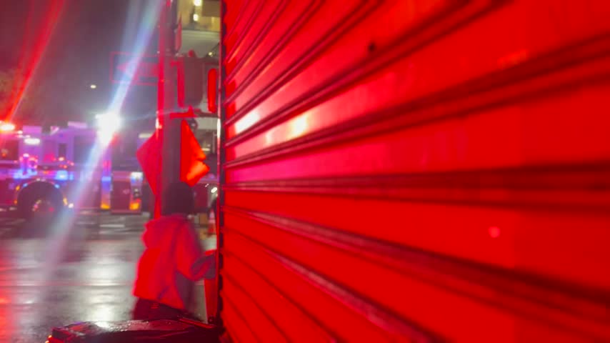 Cinematic close-up of a red metal roller door at night with urban street lights and reflections creating a moody atmosphere.
