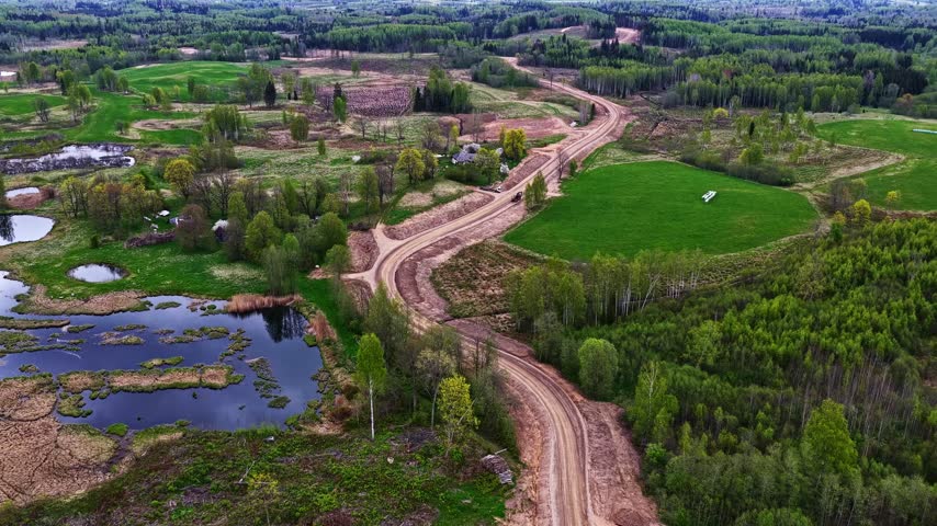 Aerial footage showing a new winding gravel road under construction through a verdant countryside