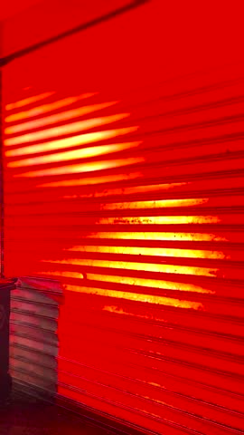 Cinematic close-up of a vibrant red metal roller door in an urban night setting, showcasing industrial texture and city atmosphere.

