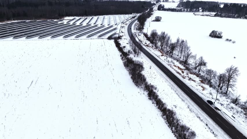 Top-down view of a solar farm and a winding road amidst a snowy, minimalist rural landscape
