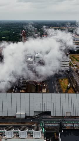 Thick steam rises from large industrial chemical plant with storage tanks and pipelines near Geel in Antwerp province, Belgium
