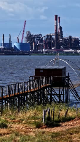 Traditional fishing hut contrasting with an industrial petroleum refinery in France