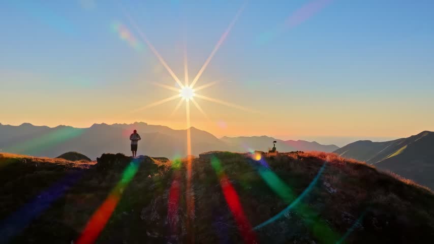 Hiker watching a spectacular mountain sunset with a vibrant sunstar lens flare at Col d