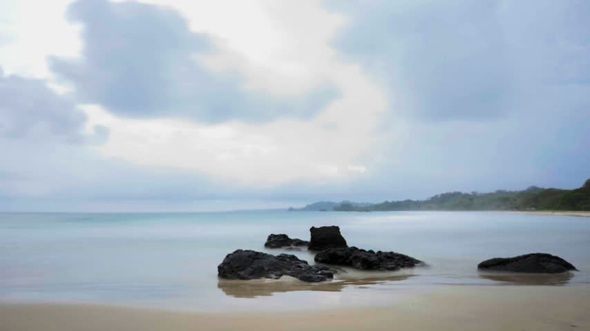 Cool blue clouds drift above an ocean shoreline as evening sets over wet coastal sand.