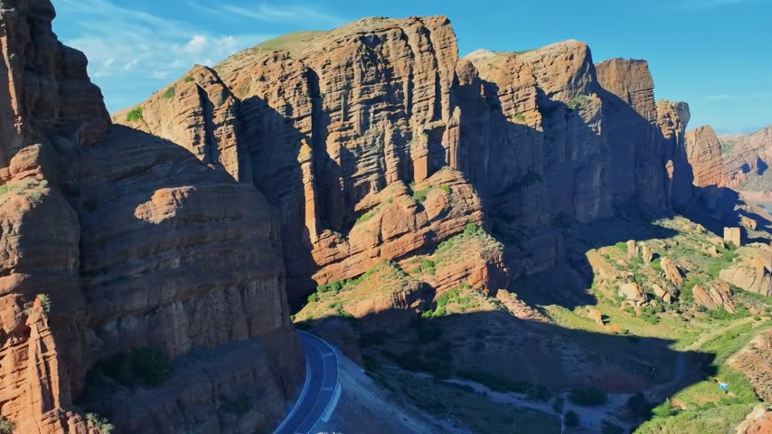 An aerial perspective showcases a dramatic road winding through majestic red rock canyon formations under a clear blue sky.