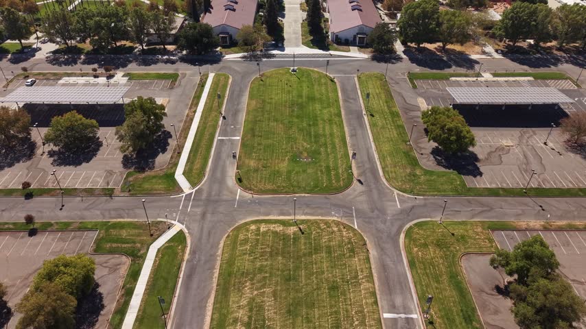 Top-down aerial view slowly flying over the modern campus of Woodland Community College in California, revealing its symmetrical layout, manicured lawns, parking lots, and academic buildings