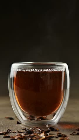 Amber cascara infusion rests in wide double wall glass cup beside coffee cherry husks in closeup.