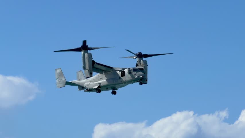 A military tiltrotor aircraft flies through blue skies with white clouds over Gold Coast, Australia.