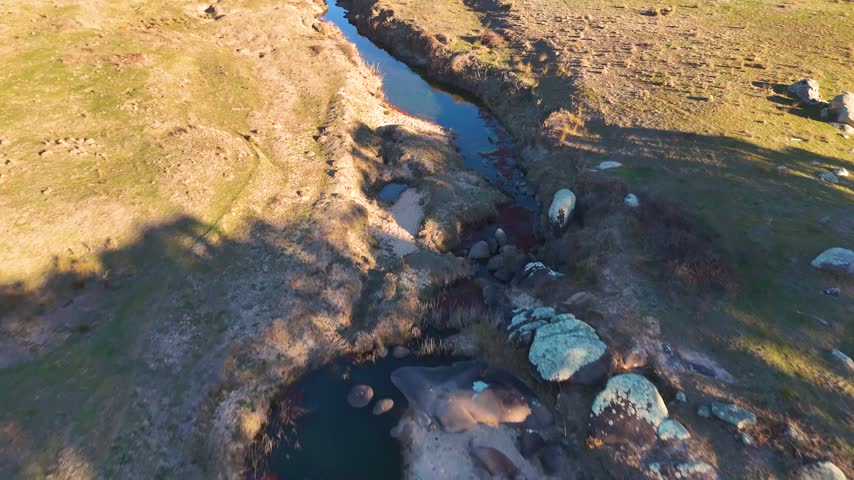 An aerial shot tracking over a winding rural creek surrounded by granite boulders in Australia.