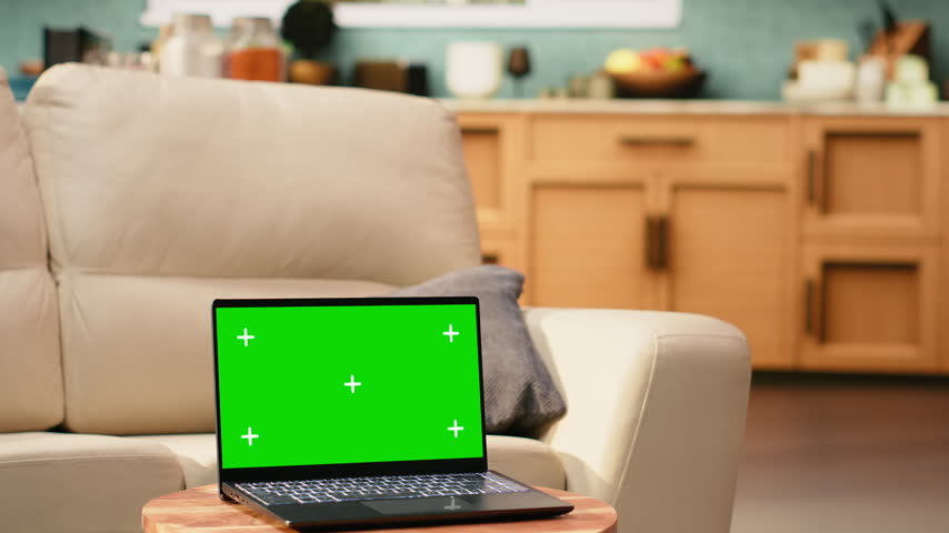 Green screen mockup on laptop in empty modern living room, device placed on wooden coffee table, with no people indoors