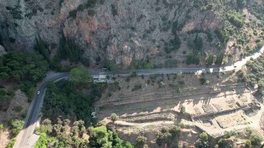 Aerial view of the ancient ruins of Delphi nestled in the mountainside with a winding road and lush trees in Delphi, Greece.