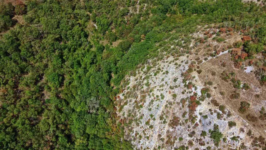 Top-down drone shot over rocky, shrub-covered limestone hillside borders Occitania region terrain with hidden winding Lot River, France