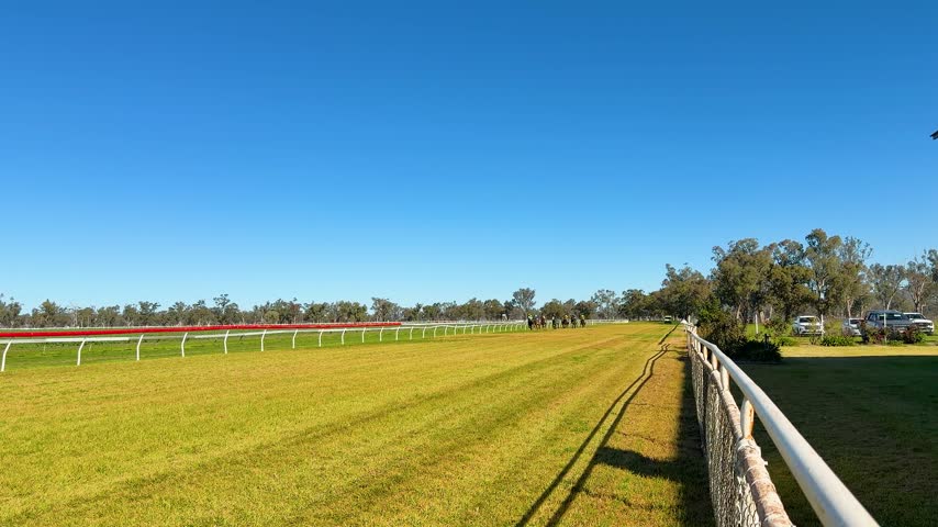 Wide shot of jockeys racing thoroughbred horses on a sunny grass track in Gunnedah, Australia.