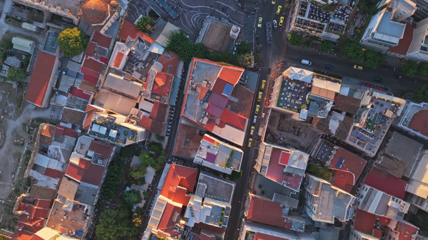 Stunning aerial top-down perspective rotating above Monastiraki square in Athens, Greece, showing the ancient urban center with historic buildings and bustling streets at sunset