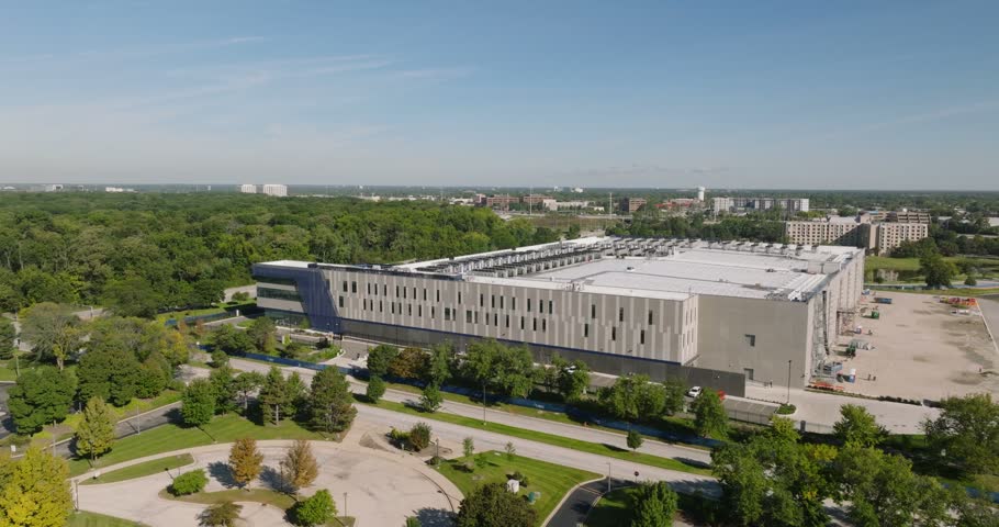 Aerial view of a modern data center building surrounded by lush green trees and parking areas in Elk Grove Village, Illinois, United States.