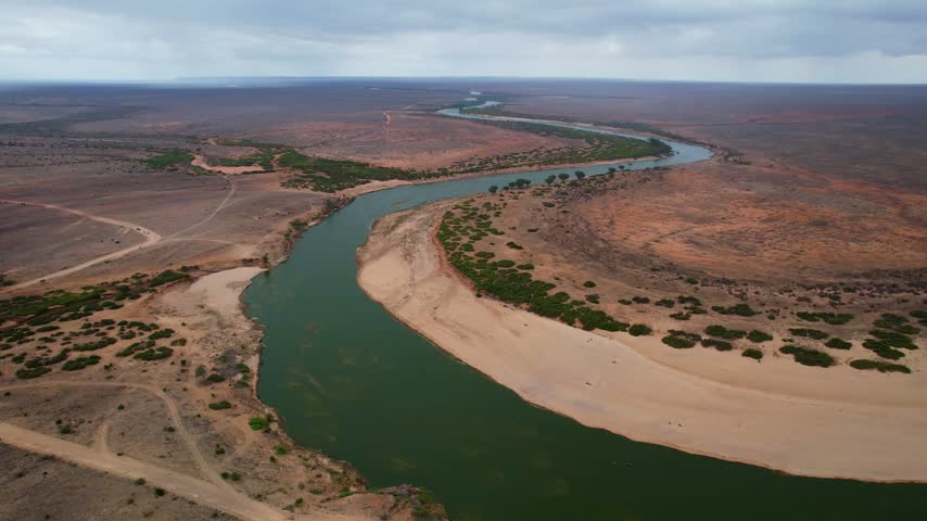 Aerial view of the winding Galana River flowing through the arid landscape of Tsavo East, with sandy banks and sparse green vegetation in Tsavo East, Tana River County, Kenya.