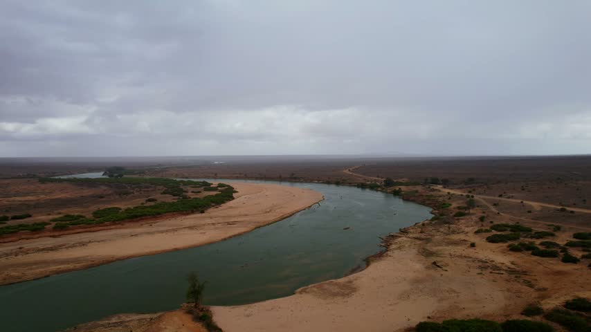 Aerial view of the winding Galana River flowing through the arid landscape under a cloudy sky in Tsavo East, Tana River County, Kenya.