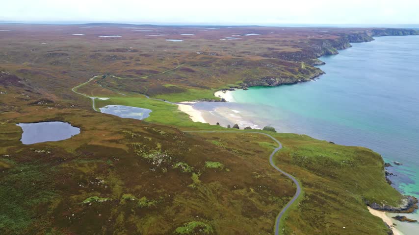Aerial view of remote coastline with sandy beach, winding road, and rugged moorland
