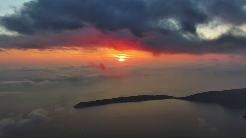 Aerial view of a vibrant sunset over the Adriatic Sea with clouds and calm water in Montenegro.