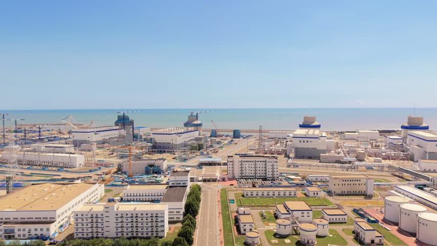A large coastal industrial complex with multiple buildings and structures, adjacent to the sea under a clear sky.